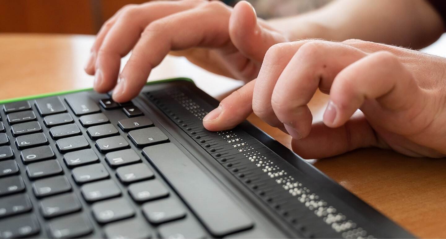 Zeigt einen Menschen an einem Laptop für Blinde mit Braille-Zeilen